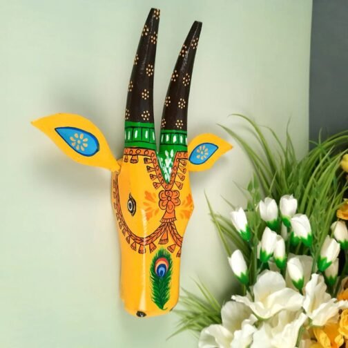 A colorful hand-painted wall mask with yellow as the dominant color, featuring traditional decorative patterns, floral designs, and a central peacock feather motif. The mask has blue and green accents, adding a lively and artistic touch to home decor.