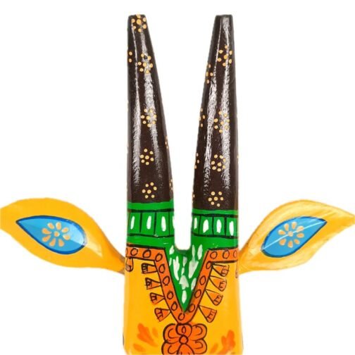 A hand-painted wall mask with two tall black horns, green detailing, and blue-accented yellow ears. The mask is adorned with intricate traditional patterns and floral designs on a yellow base, adding a vibrant and artistic touch to any wall decor.